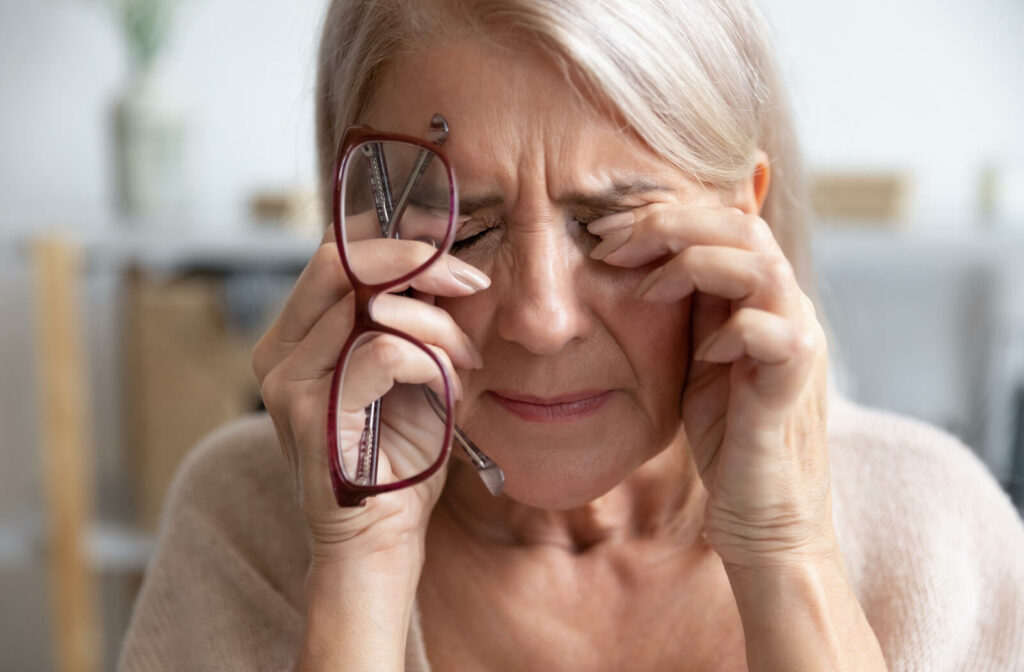 a woman rubs her eyes while holding her glasses because of blurred vision