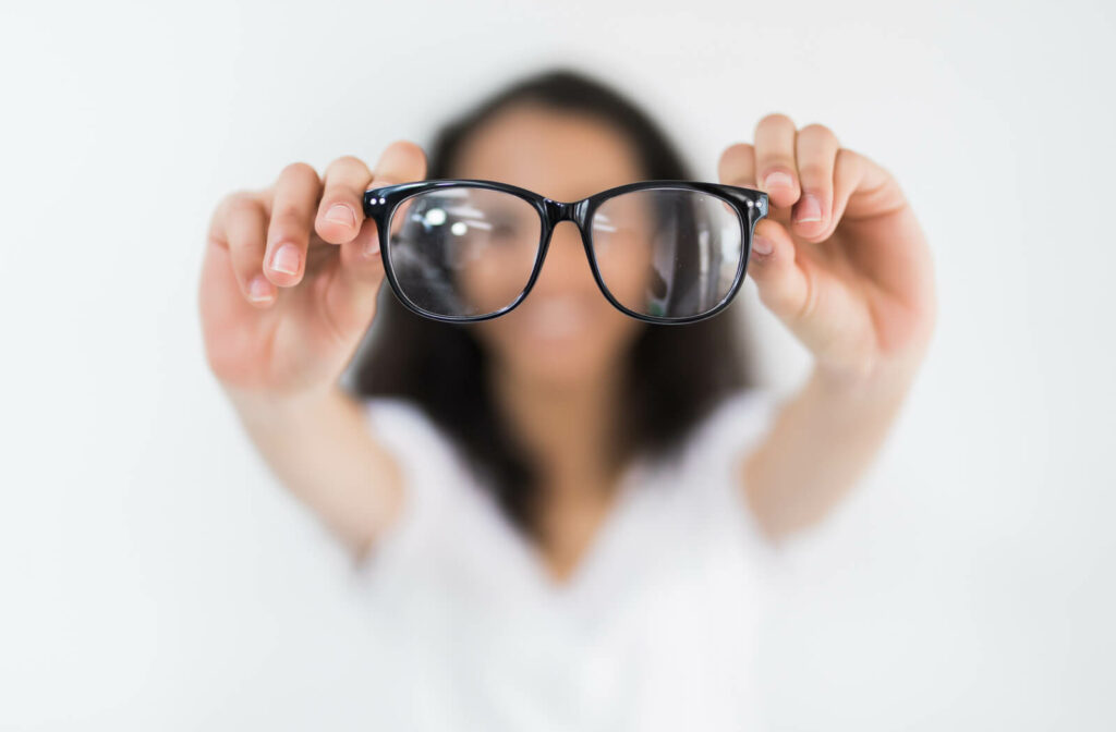 a woman stands holding glasses towards the camera. the image is blurred except the glasses