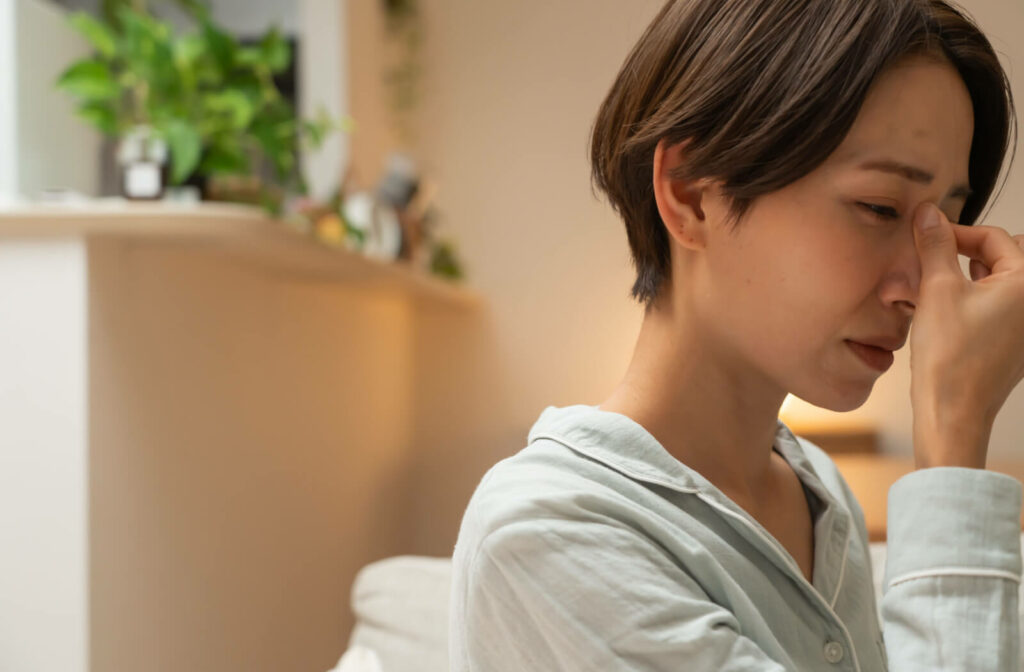 A woman woke up with dry eyes after sleeping with contact lenses on.  She's pressing the part between her eyes above the nose with a gesture of irritation on her face.