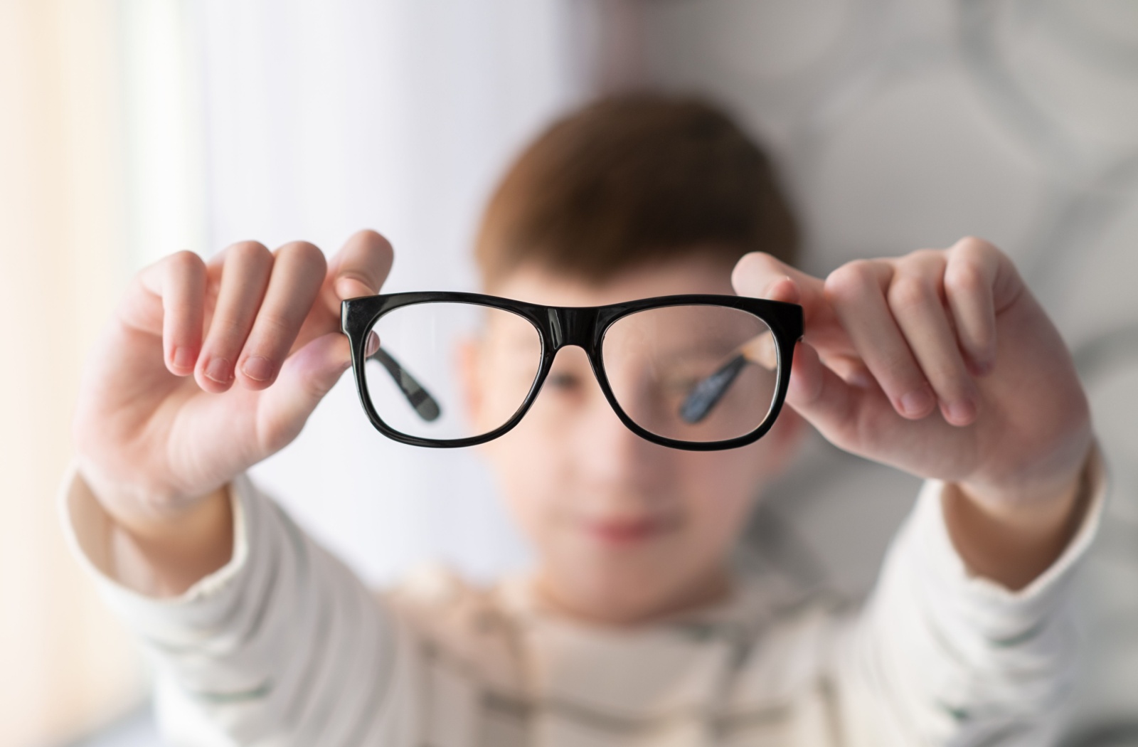 A young child holds myopia control glasses in front of them with outstretched arms.