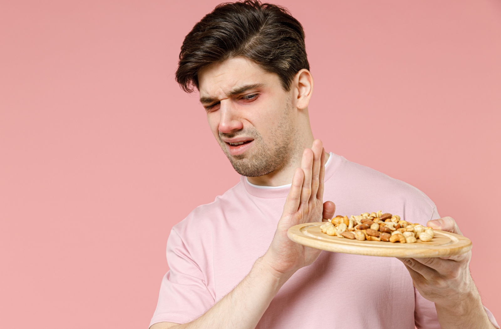 An adult with red eyes making a disgusted expression while refusing a plate of mixed nuts.