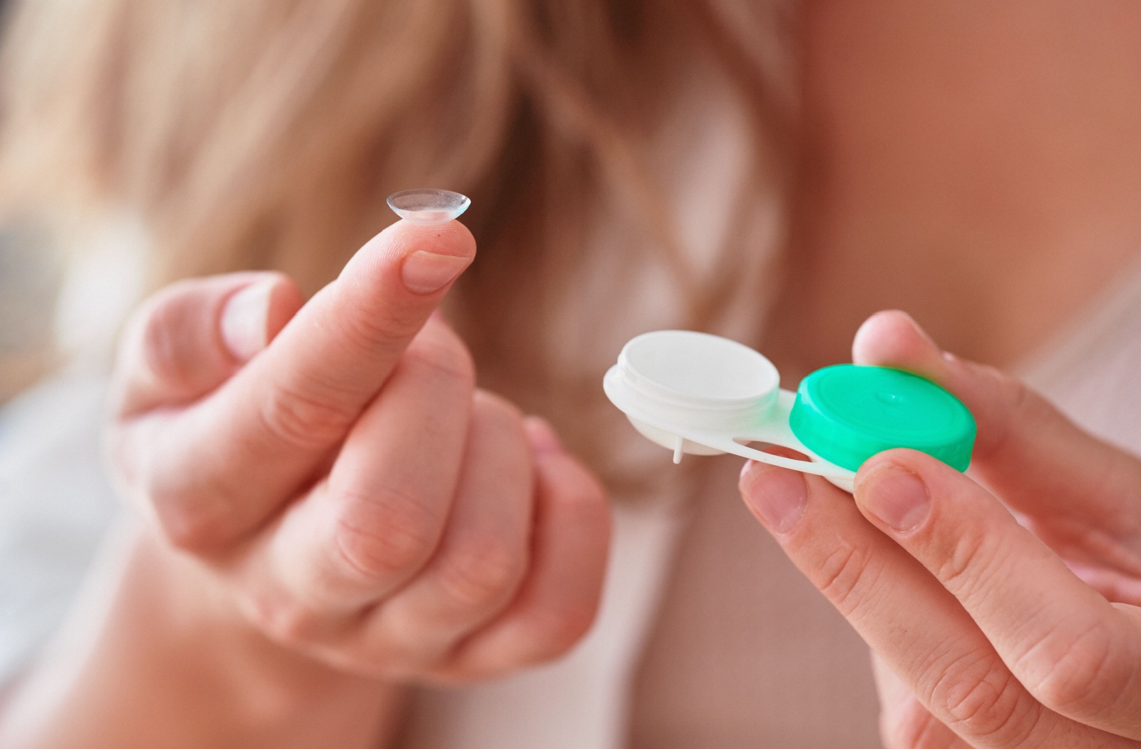 A zoomed-in image of a person holding their contact lens case with a single lens on the tip of one finger.
