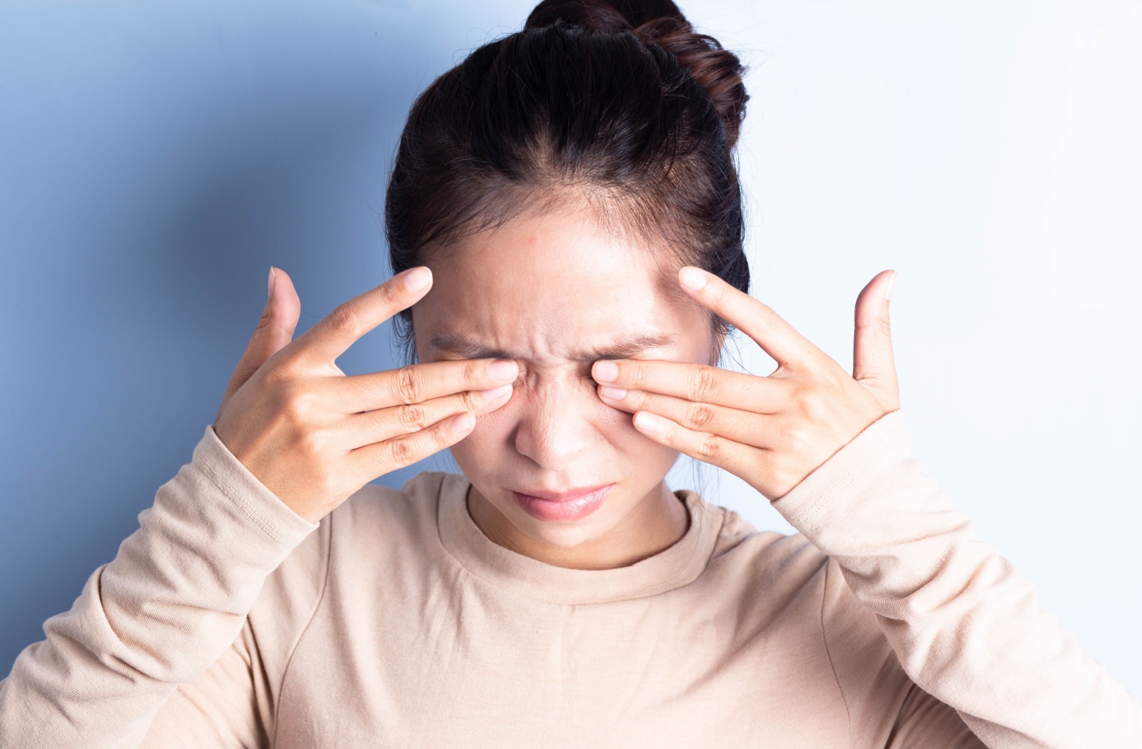 A young adult rubbing their eyes with both hands in frustration from their dry eyes.