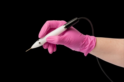 Hand wearing a pink medical glove holding a handheld plasma pen device against a black background.