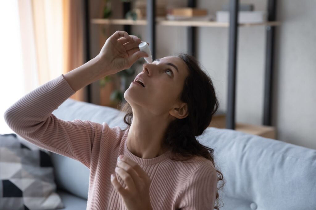 Woman on couch putting eye drops.